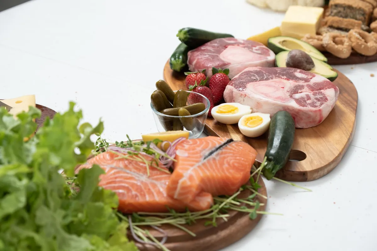 Surtido de alimentos keto como salmón, carne y verduras sobre tablas de madera.