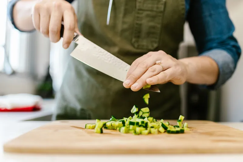 Manos cortando verduras frescas sobre una tabla de madera en casa