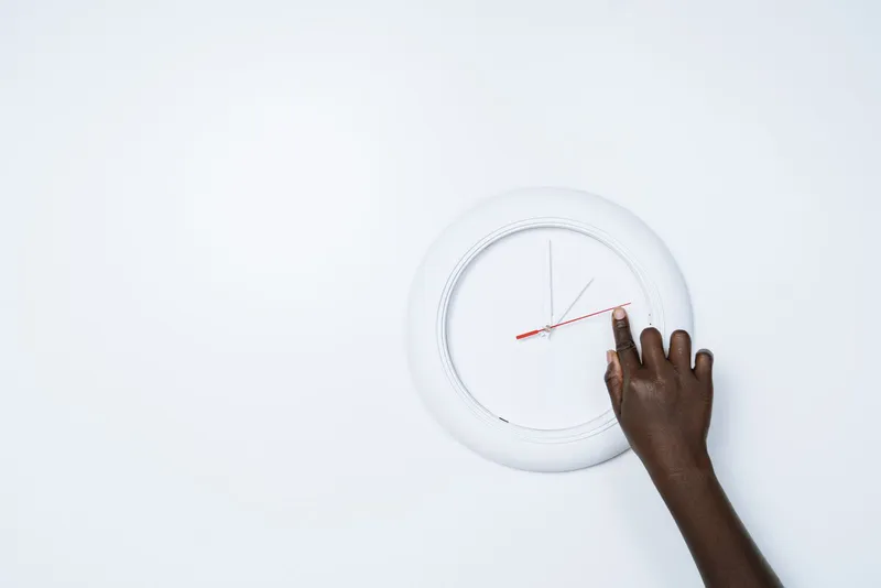 Mano ajustando un reloj de pared que marca la ventana horaria de comidas del ayuno intermitente