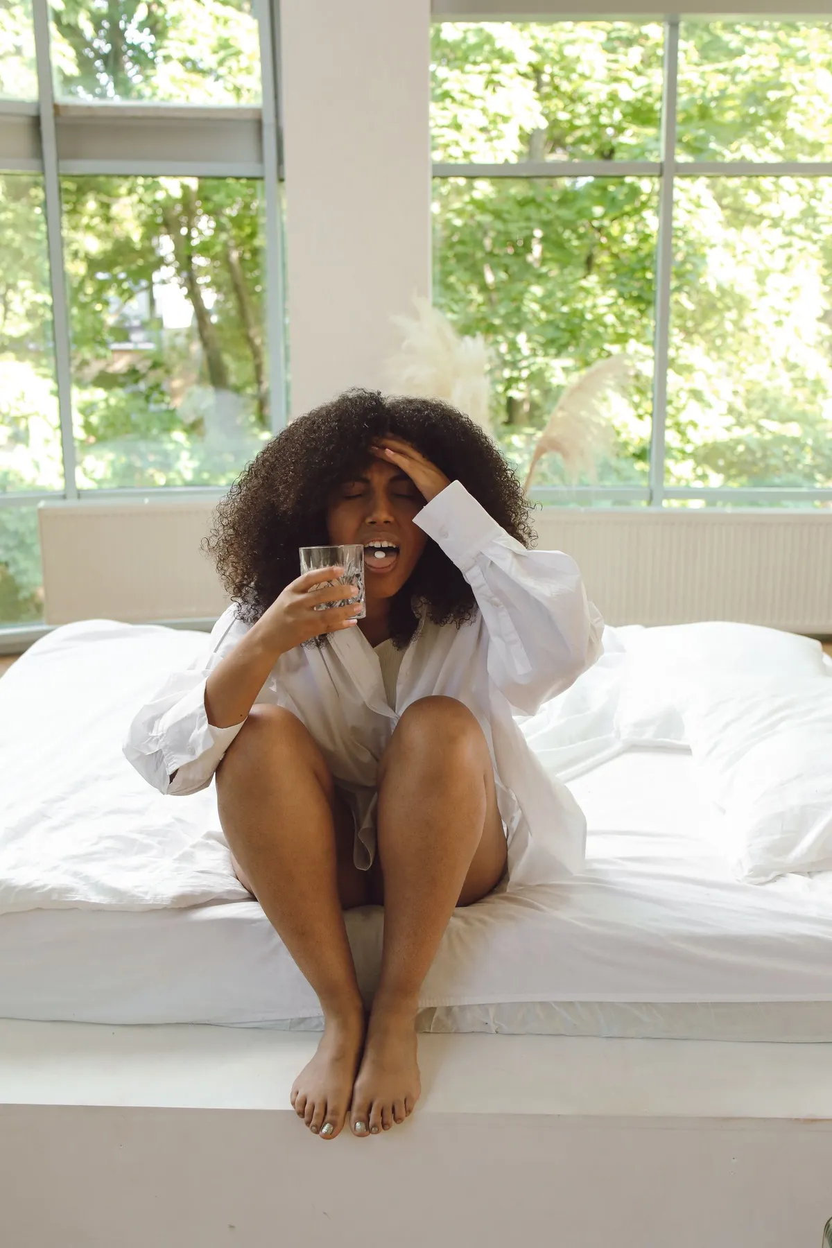 Mujer sentada en la cama con un vaso de agua sufriendo dolor de cabeza por la gripe keto