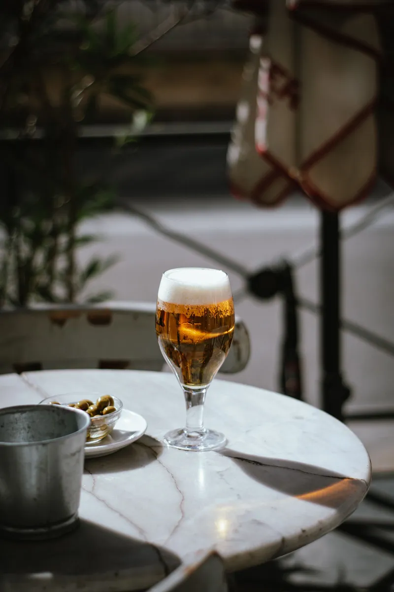 Caña de cerveza con aceitunas sobre una mesa de mármol en la terraza de un café de Madrid